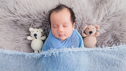 Cute baby wrapped in blue blanket peacefully sleeping with plush toys
