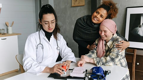 A doctor consults a cancer patient and her supportive friend in a warmly lit clinic room