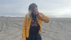 Kyla wearing a yellow jacket and standing on sand.