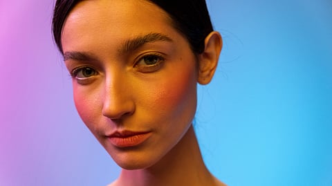 A woman with a glowing face and purple and blue background behind.