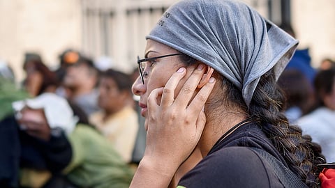 A woman with scarf on head and hand touching her ear. 