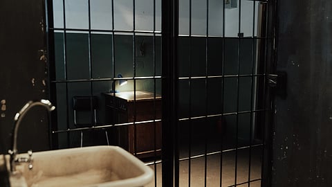 A prison with a chair and table inside and a sink on the left.
