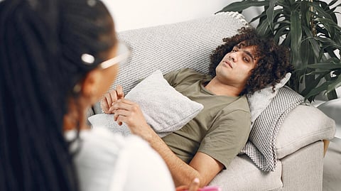 Man lying on couch during therapy session with female therapist taking notes