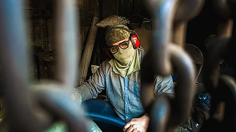 A masked industrial worker seen through hanging chains, focused on safety in a workshop environment