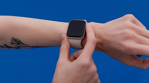 A person adjusting a modern smart watch against a bright blue background
