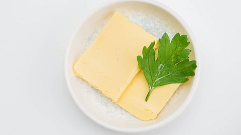 Top view of butter slices garnished with a parsley leaf on a white plate for culinary presentation