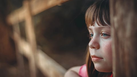 Young girl with blue eyes gazing thoughtfully outdoors by a wooden fence
