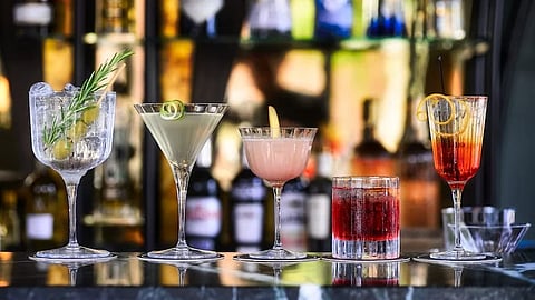 Five elegant cocktails sit on a shiny bar counter, garnished with herbs and citrus.