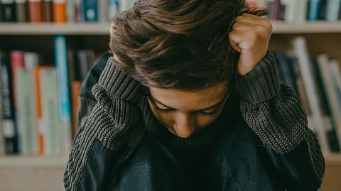A young person sitting in a thoughtful, introspective pose in a library setting