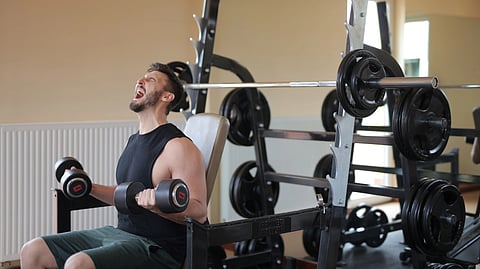 Man straining while lifting dumbbells in gym for strength training