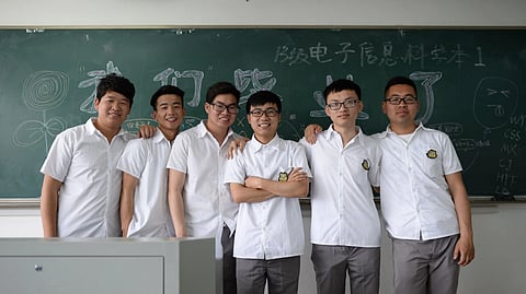 Six male students pose in a classroom in front of a chalkboard
