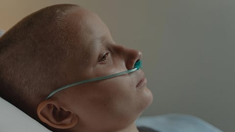 A bald woman with nasal cannula lying down, reflecting illness and solitude