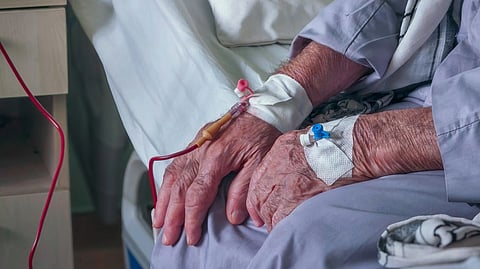 An old man sitting in a hospital bed with a cannula on both hands.
