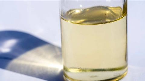 A close-up image of a glass bottle with liquid, showcasing light reflection and shadow on a white surface