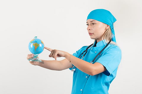 Female travel nurse putting finger on globe to choose destination in blue uniform.
