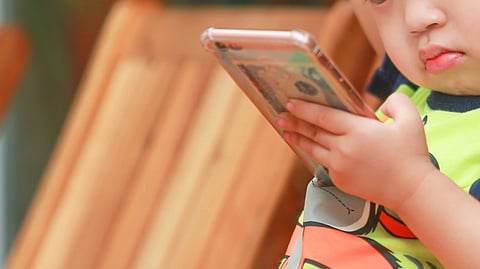 boy holding smartphone while sitting on a chair