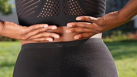 A woman in black sports wear with hands on her back.