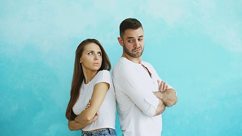A couple in white t-shirts standing facing away from each other and looking mad.