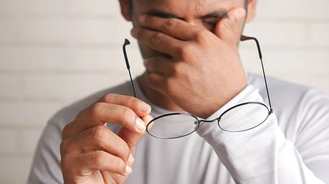 A guy holding spectacles in one hand and the other hand on his eyes. 