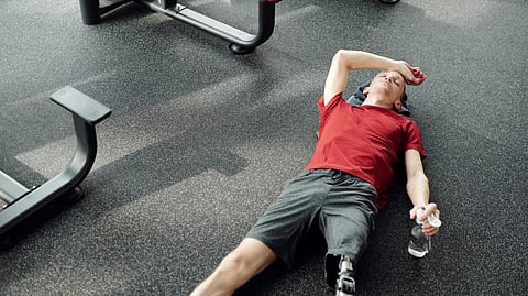 A man with a prosthetic leg rests on the gym floor, holding a water bottle after an intense workout