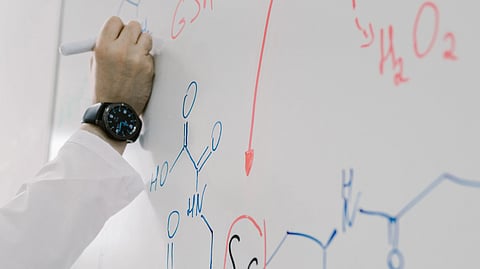 person wearing a lab coat writing formula on white board