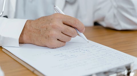Close-up of a doctor's hand writing notes with a pen on paper, capturing a moment in a medical setting