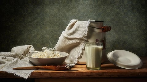 A rustic still life featuring cottage cheese in a bowl, a glass of milk, and kitchenware on a wooden table