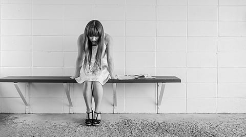 A girl sitting on a bench and looking down.