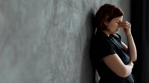 A woman in stress with eyes closed, leaning against a concrete wall indoors