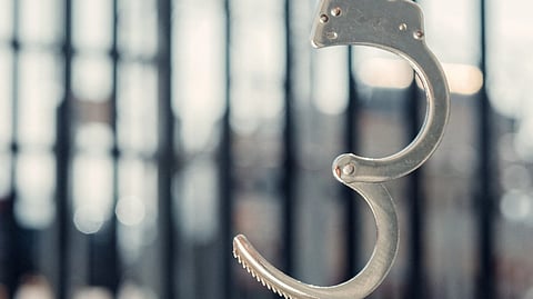 A handcuff opened, and a background of prison bars.