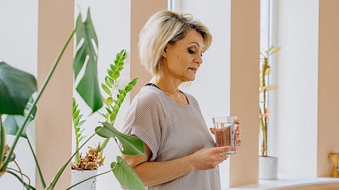A woman holding a glass and standing next to plants.