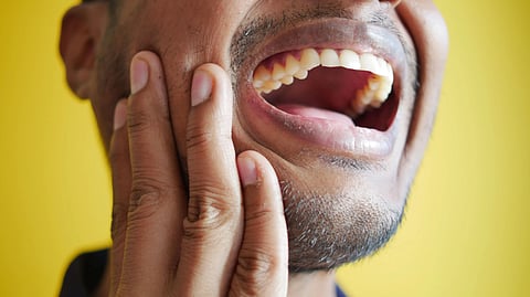 Close-up of a man holding his cheek, displaying a wide open mouth against a yellow background