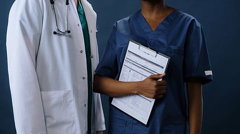 Two healthcare professionals in scrubs and lab coat with a clipboard, representing teamwork