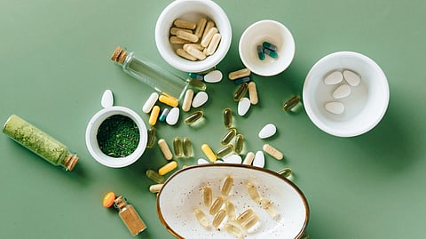 Top view of various herbal and pharmaceutical supplements in ceramic bowls on a green background