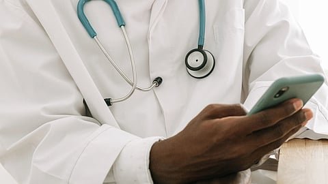A doctor with a stethoscope and holding phone in hand.