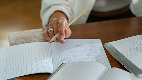 person sitting on wooden table holding a pencil