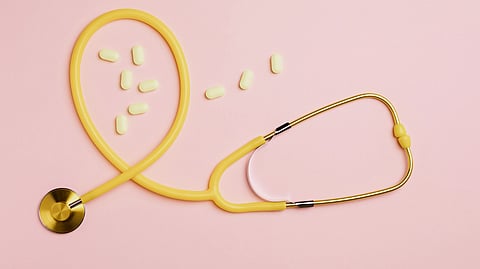 A yellow stethoscope with pills on a pink flat lay setting, symbolizing medical care