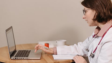 A doctor holding a pen and using a laptop.