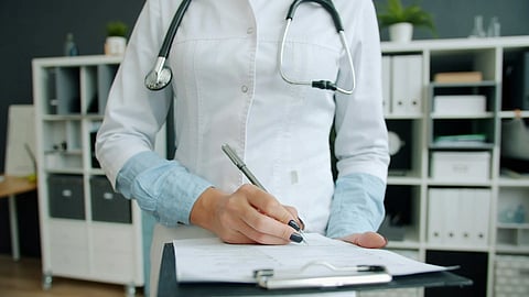 Close-up shot of hand of nurse writing in patient's medical records ticking symptoms working in hospital office. 