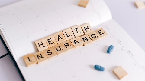 Close-up of health insurance spelled out with Scrabble tiles on a planner, alongside medication pills