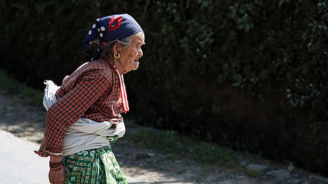 An elderly woman wearing a head scarf and traditional dress walking on a sunny day