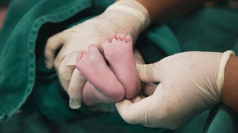 A newborn's feet being gently held by a nurse in latex gloves in a hospital environment