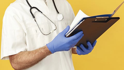 A doctor with a stethoscope around their neck and holding a writing pad.
