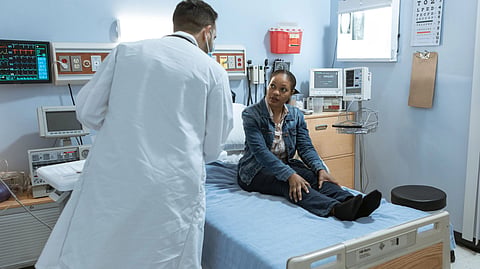 A doctor consults with a patient in a medical facility room, surrounded by healthcare equipment