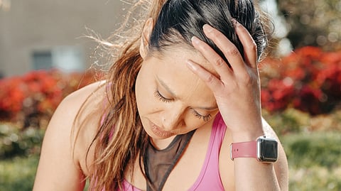 Close-up of a woman with a headache sitting outdoors wearing a smartwatch