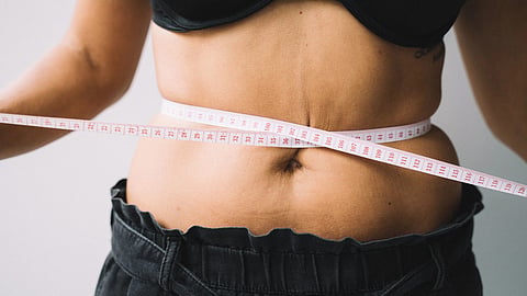 A person measuring their waist with a tape, symbolizing fitness and health goals
