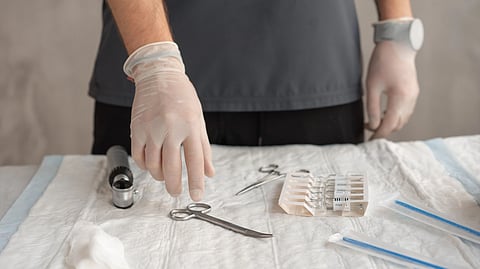 A surgeon wearing medical gloves and picking up surgical equipment.