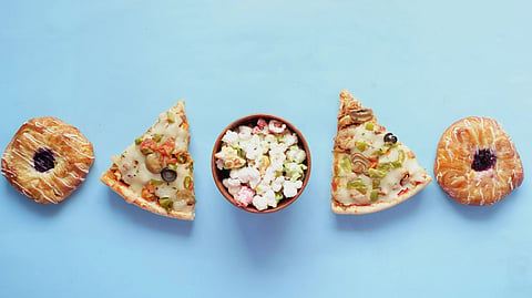 2 slices of pizza, doughnuts, and a bowl of popcorn kept in a line on a blue background.