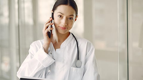 A female doctor holding a phone and has a stethoscope around neck.