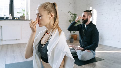 Two individuals practicing mindful breathing yoga in a serene indoor home setting